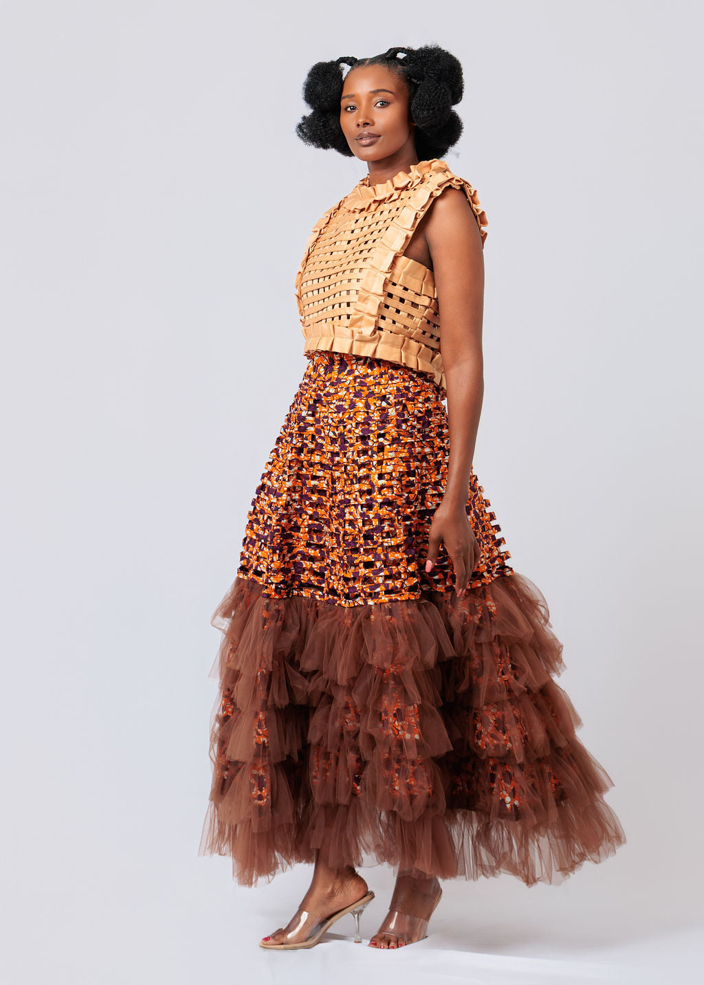 Woman wearing a gold top and brown ruffled skirt on a white background