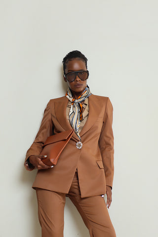A woman wearing a light brown suit jacket with a classic cut, paired with a striped tie and sunglasses.