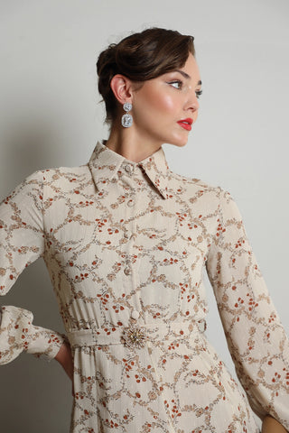 A woman wearing a beige floral dress with long sleeves and a round neckline.