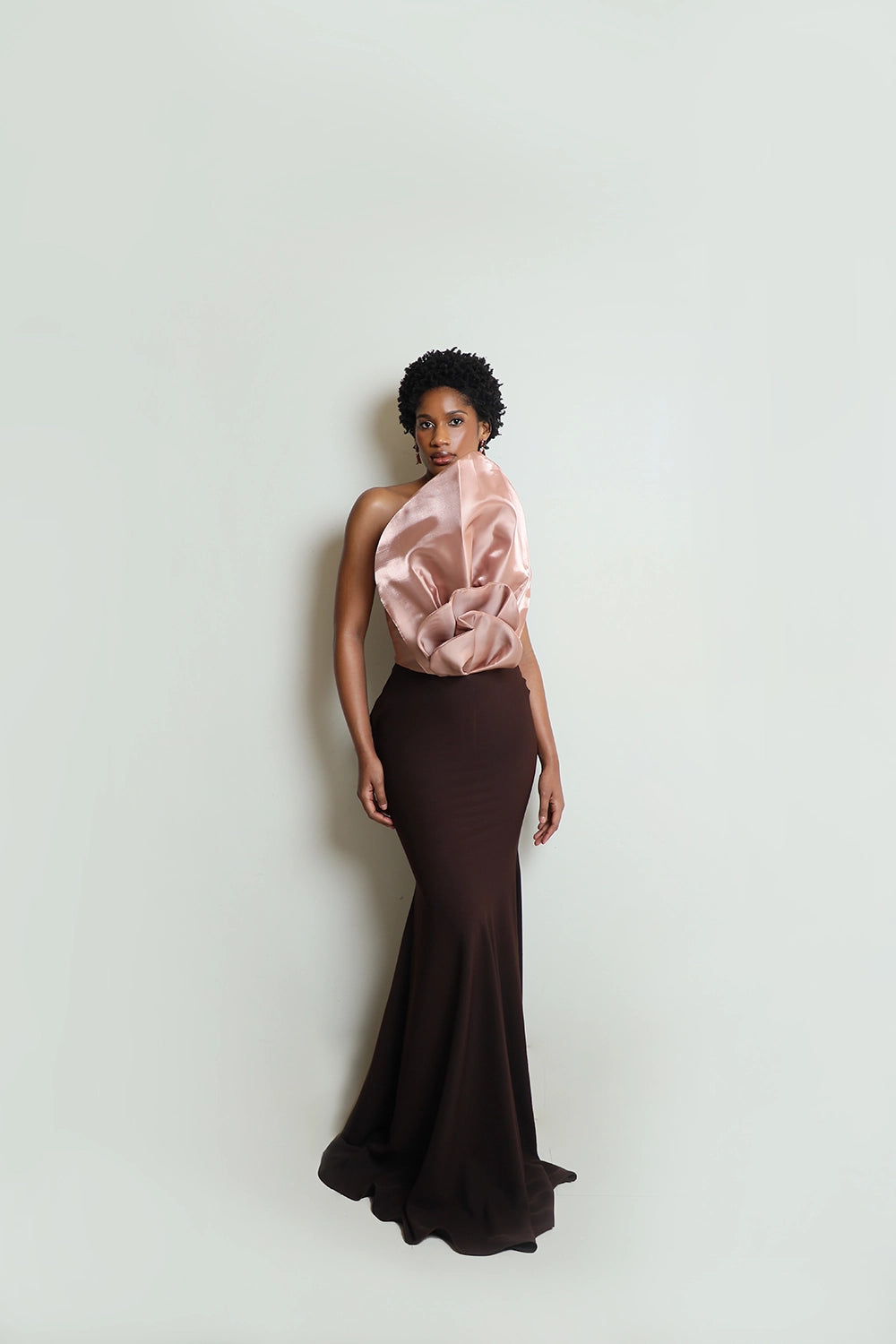 A woman wearing a floor-length brown dress with a glimmering brown blooming flower bodice, posing against a neutral background.