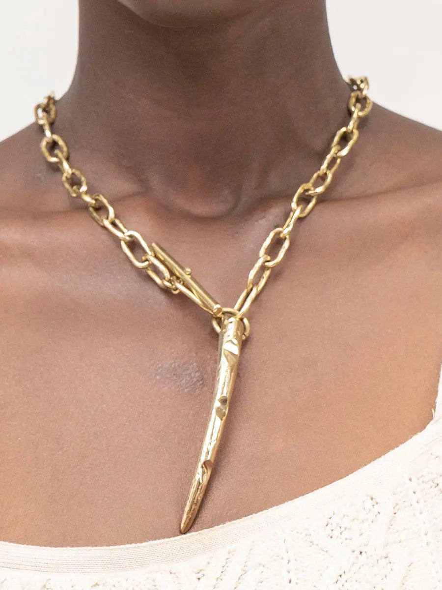 Gold chain necklace with a unique pendant on a person against a neutral background