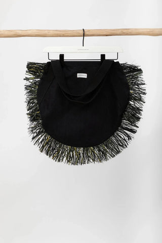 Black fringed bag hanging on a wooden rod against a white background