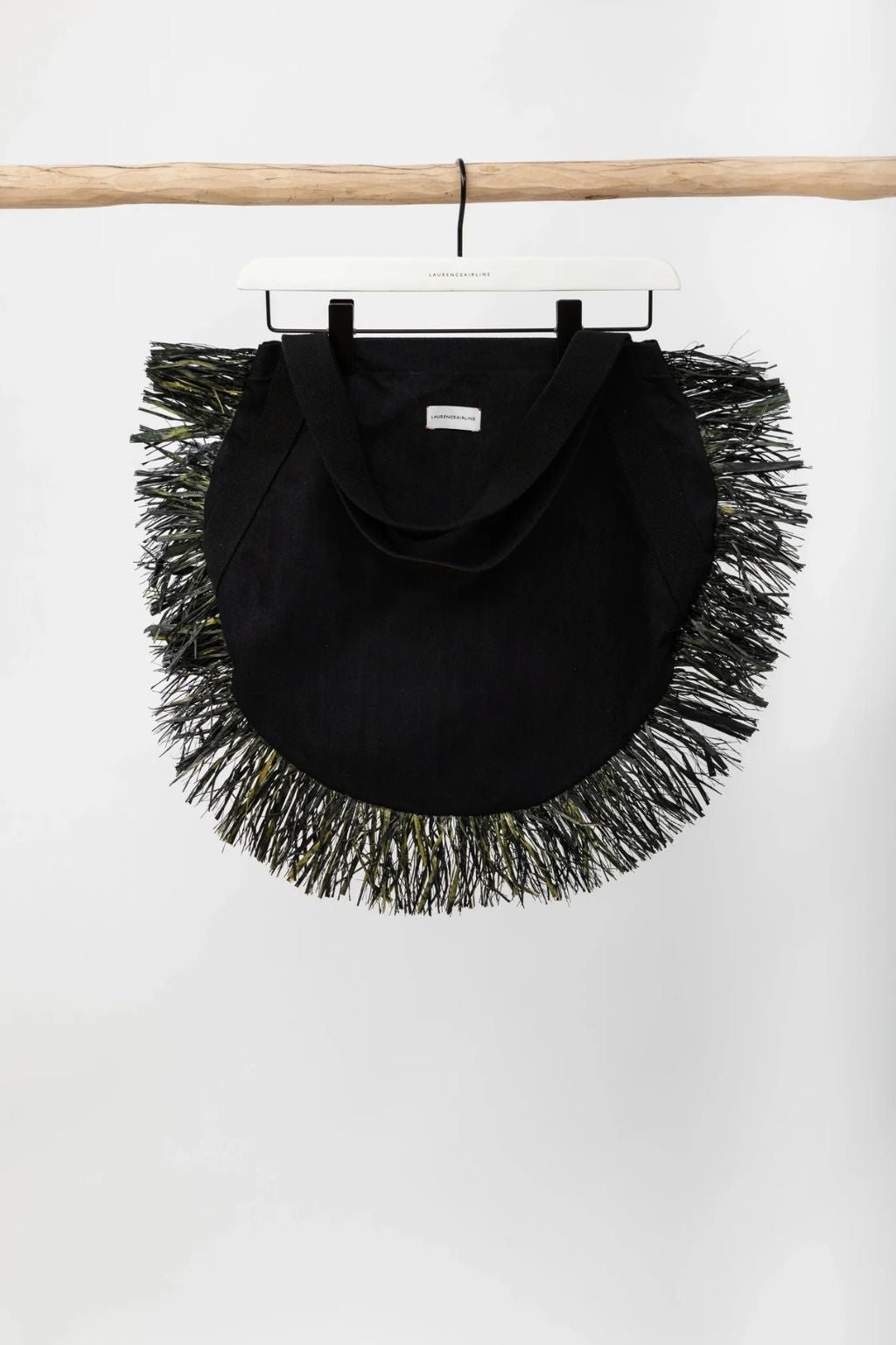 Black fringed bag hanging on a wooden rod against a white background