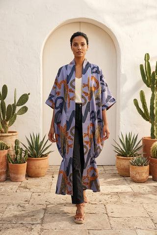Woman wearing a patterned kimono standing in front of a white wall with cacti.