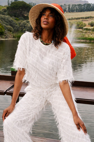 Woman in a white outfit with fringe sitting by a lake