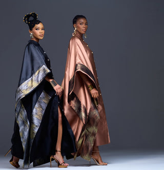 Two models wearing traditional African-inspired capes (Ankara) in black and dusty rose, featuring metallic patterned borders, posed against a dark gray studio background for House of NALA.