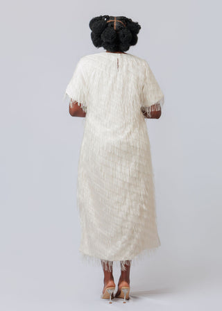 Person wearing a white lace dress with fringe details on a plain background