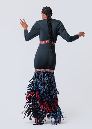 Person wearing a dark gray long-sleeve top and colorful fringed skirt on a white background