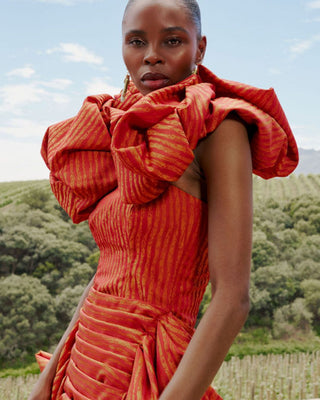 Woman wearing an orange evening dress with a textured pattern in an outdoor setting by NALA Privé at House of NALA. 