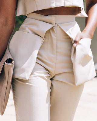 A model wearing a beige cargo suit with pants and a sleeveless top, accessorized with sunglasses and a clutch.