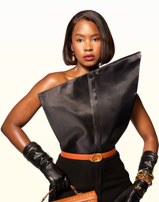 Woman wearing a black one-shoulder top with a brown belt and gloves on a white background