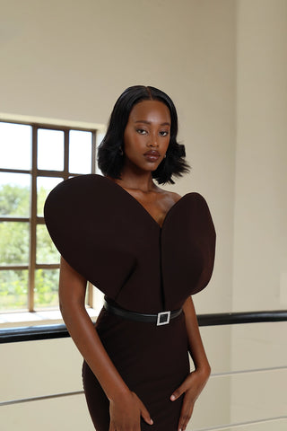 A woman wearing a brown, figure-hugging dress with a 3D heart detail on the front, standing indoors.