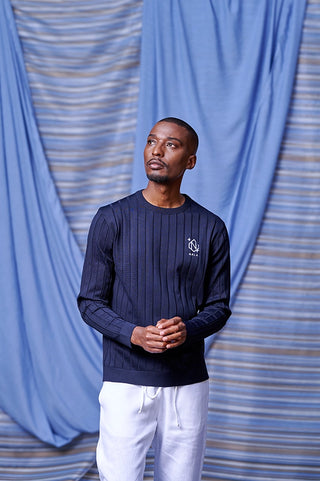 Man wearing a navy blue sweater with a logo against a blue curtain background