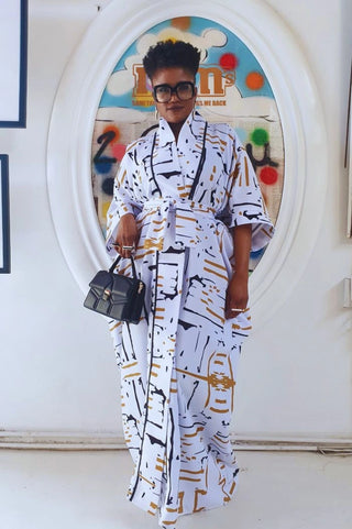 Person wearing a white patterned outfit with a black handbag in front of a colorful door.