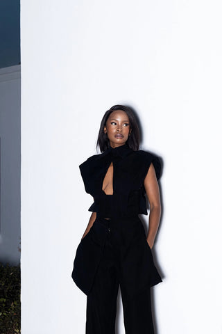Person wearing a black outfit with a unique design, standing against a white wall. Pre-Order at House of NALA Sandton City